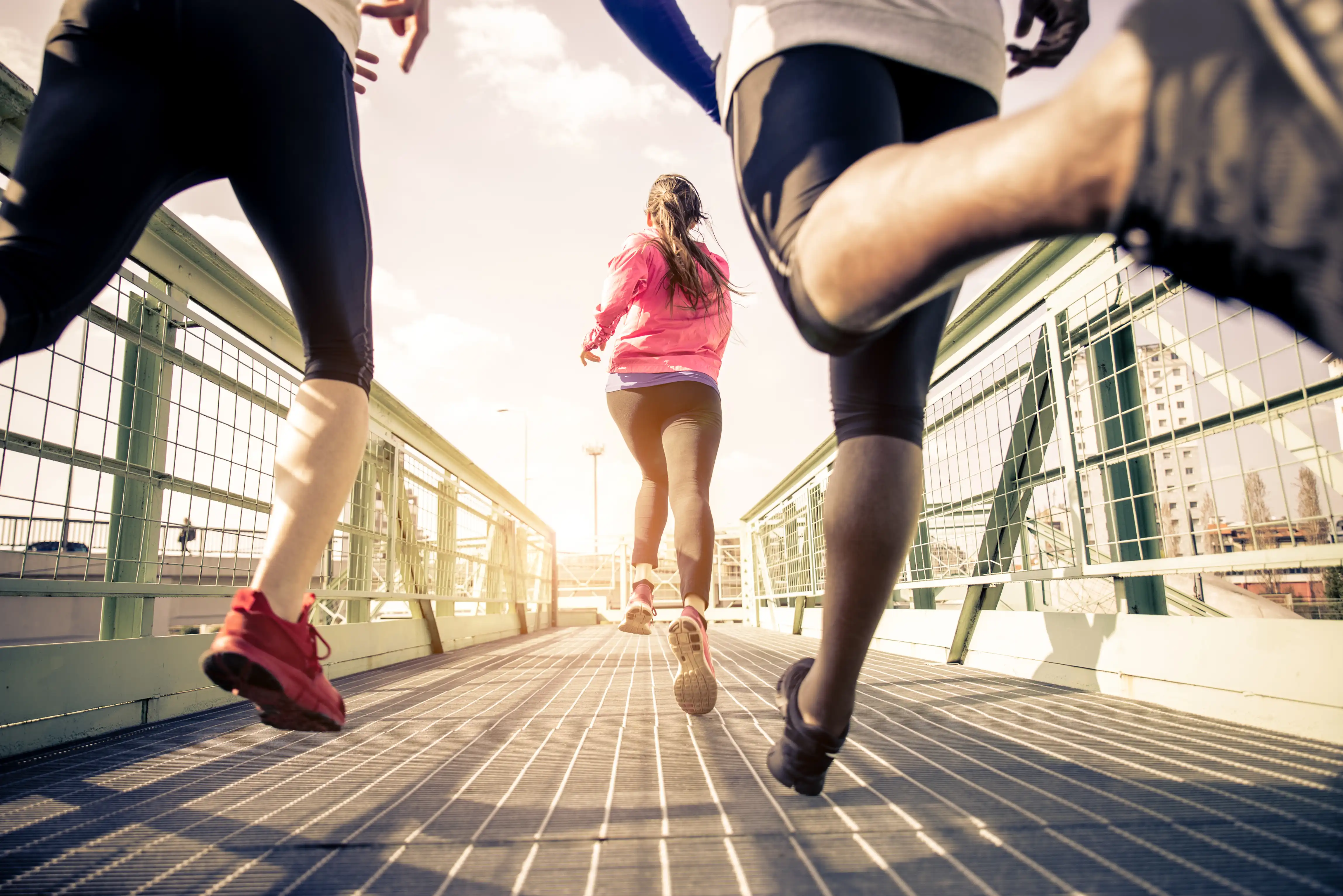 three runners sprinting on a bridge - one pulls ahead